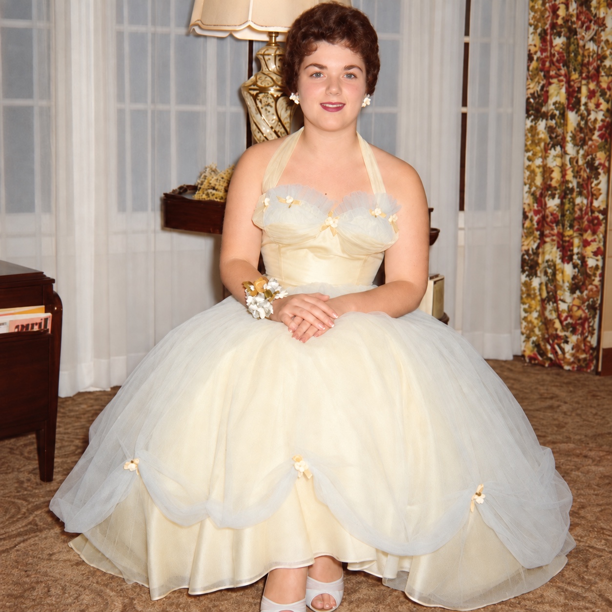 Judith seated in a full pale yellow and blue gown with small flowers, her hands folded in her lap.