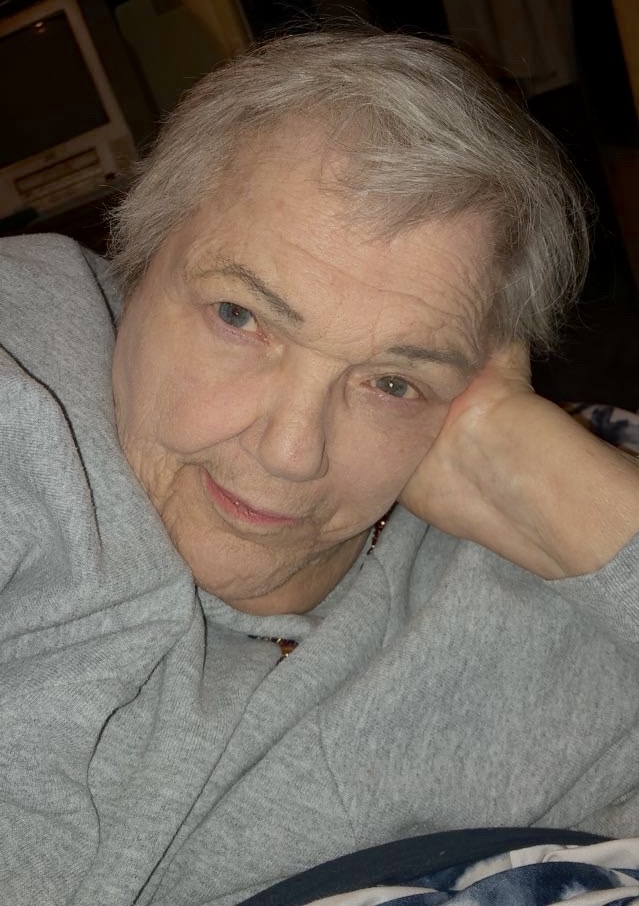 Judy in a gray sweatshirt, resting her head on her hand and looking toward the camera.